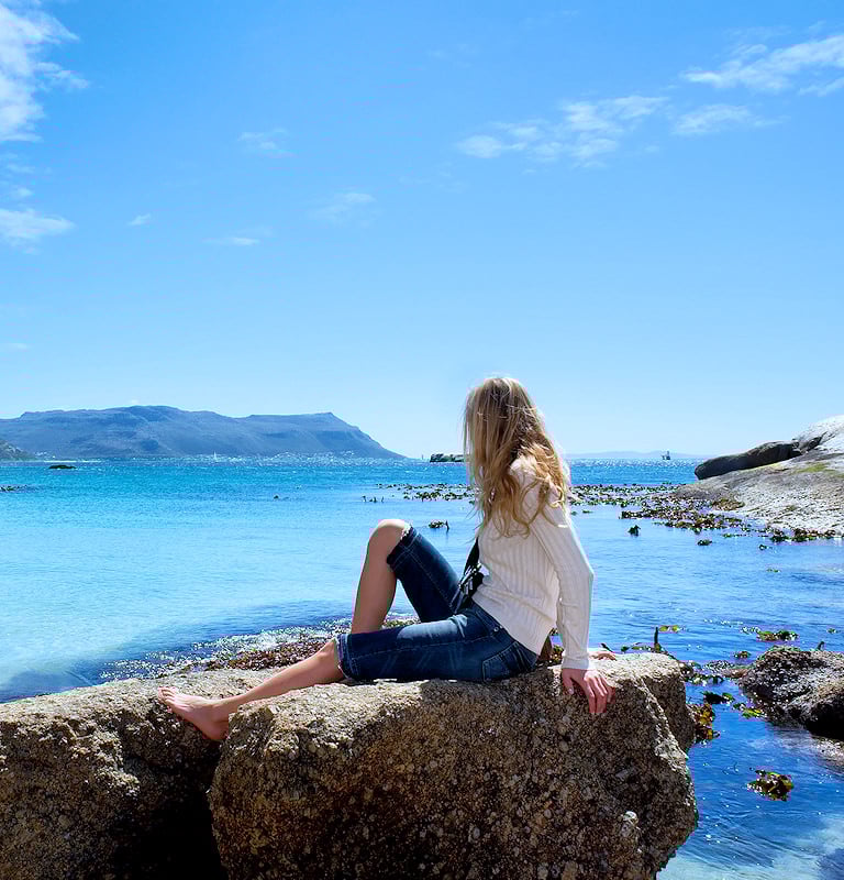 Woman sitting on rock, overlooking Walker Bay on South Africa's whale route